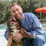 Male staff member hugging his dog in front of wade pool